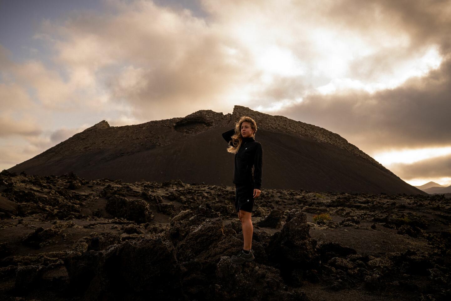 A blonde woman standing in front of a rocky mountain, dressed in Siroko Adventure clothing