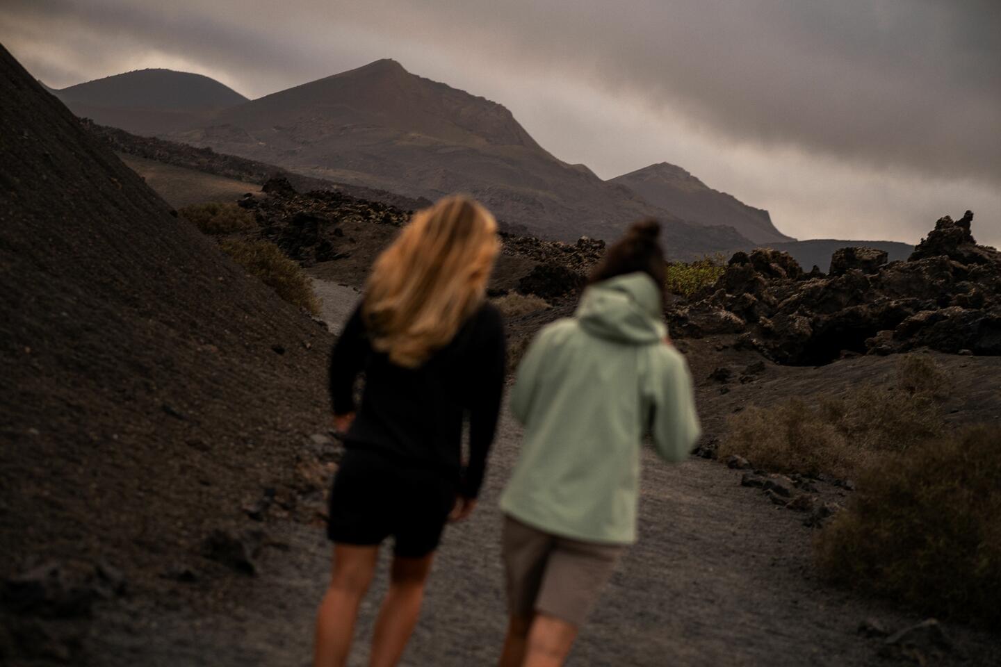 Two women seen from behind, walking along a path towards the mountain and dressed in Siroko Adventure clothing